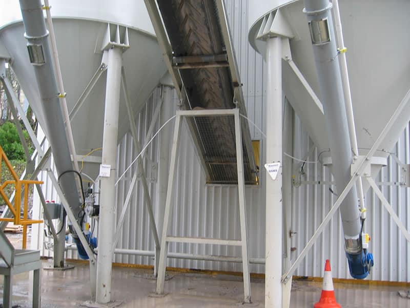 Industrial site with large metal silos and conveyor system.