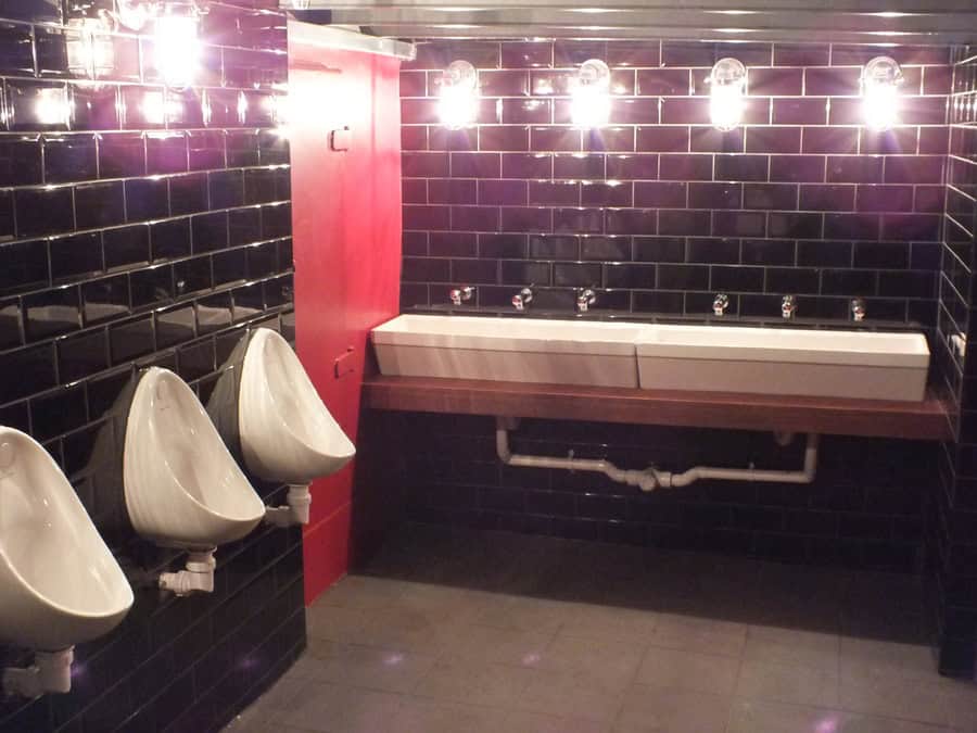 Modern restroom with black tiles, urinals, and a double sink for hygiene and convenience.